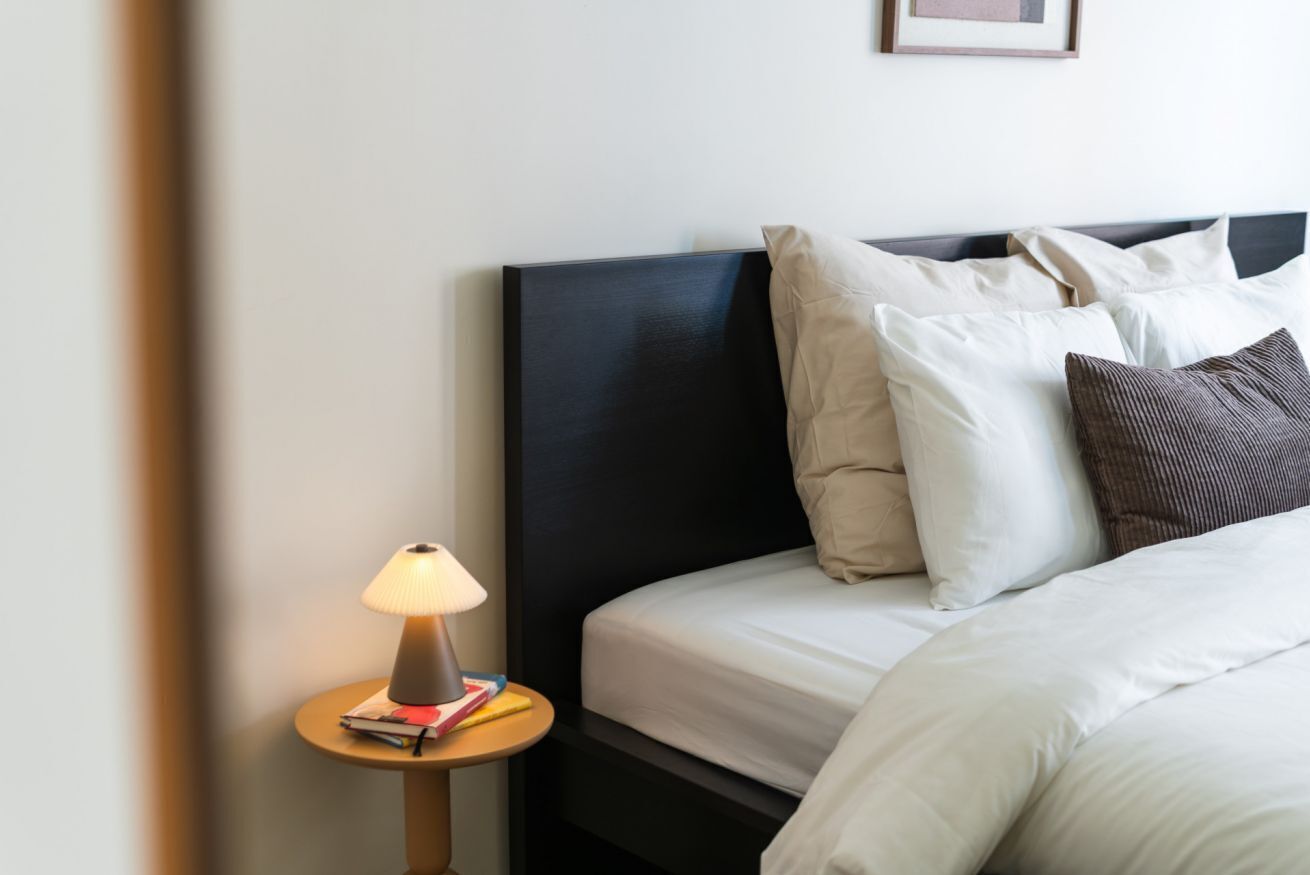 Un lit bien fait, avec des oreillers blancs et bruns, une petite table de chevet avec une lampe et un tableau encadré au mur.