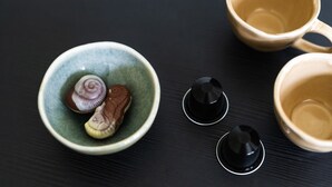 Une table en bois foncé sur laquelle se trouve un bol en céramique verte contenant deux objets décoratifs, deux boutons noirs et deux tasses en céramique beige.