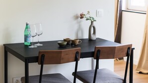 Une table à manger avec des chaises, une bouteille, des verres et un vase rempli de fleurs.