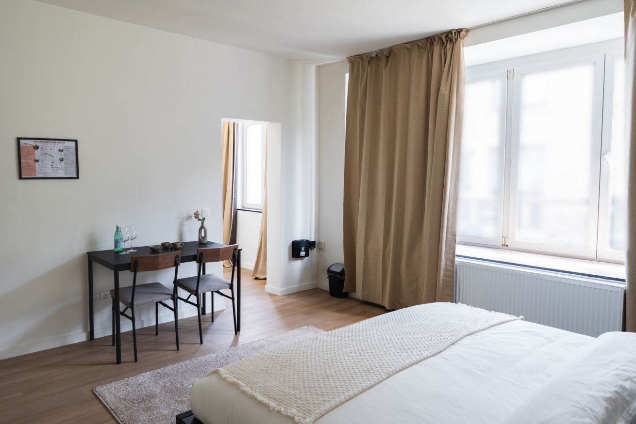 A bedroom with a bed, a desk, and a window with curtains.