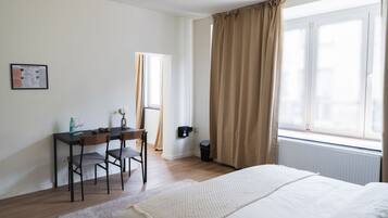 A bedroom with a bed, a desk, and a window with curtains.