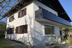 Une maison moderne à deux étages, dotée d’un toit plat, de grandes fenêtres et d’un balcon.