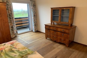 Une pièce avec un meuble en bois, un lit recouvert d’une literie à motifs floraux et une vue sur un espace extérieur, visible à travers une porte.