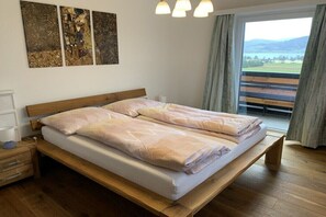 A double bed with a wooden frame, a bedside table with a lamp, and a view of a balcony with a railing.