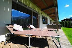 A modern outdoor lounge area with sun loungers and a wooden deck. - Holiday apartment in Lofer with swimming pool (Lofer)