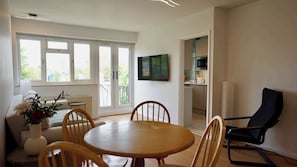 Ein modernes Wohnzimmer mit Essbereich, einem an der Wand montierten Fernseher und Blick durch Glastüren.