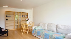 Ein Wohnzimmer mit einer Couch, einem Holzregal, einem Esstisch mit Stühlen und einer Vase mit Blumen.