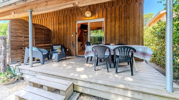 Eine Holzterrasse mit Tisch und Stühlen, ein überdachter Bereich mit einer Tür und ein kleiner Außenbereich mit einer Waschmaschine.