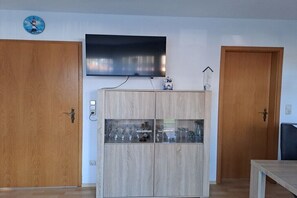 A room with a wooden cabinet, a television mounted above it, and two wooden doors. - Holiday home in Cuxhaven with swimming pool (Cuxhaven)
