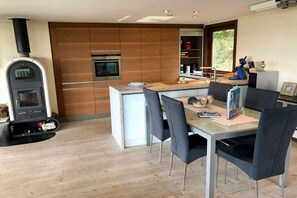 Eine moderne Küche mit Einbauofen, Holzofen und Essbereich mit Glastisch und Stühlen.