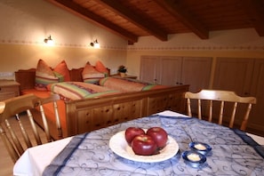 Ein gemütliches Zimmer mit einem Bett, einem Esstisch mit Äpfeln und Kerzen, Holzmöbeln und einer dekorativen Wand.