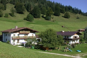 Ein zweistöckiges Gebäude mit Balkon, umgeben von grüner Landschaft und Bäumen.