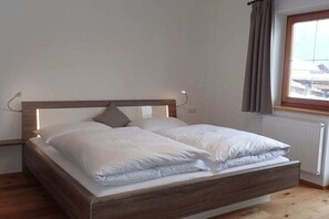 Ein Einzelbett mit Holz-Kopfstück, weißer Bettwäsche und einem Fenster mit Vorhängen.