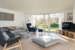 Ein modernes Wohnzimmer mit einer Couch, Sesseln, einem Couchtisch und einem Fernseher.