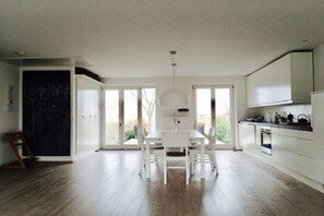 Eine moderne Küche mit weißen Schränken, einem Esstisch mit Stühlen und einem großen Fenster.
