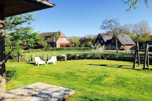 Ein Wohngarten mit einer Holzdielenveranda, zwei weißen Stühlen und einem Holztisch.