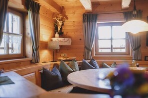A cozy wooden cabin interior with a round table, cushioned seating, and a crucifix decoration. - Alpine hut in Rauris with swimming pool (Rauris)