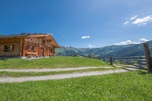 A rustic wooden building with a sloped roof, a gravel path leading to it, and a mountain backdrop. - Alpine hut in Rauris with swimming pool (Rauris)