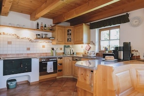 A kitchen with wooden cabinets, a stove, a sink, and a window with curtains. - Alpine hut in Rauris with swimming pool (Rauris)