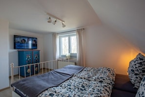 Ein Schlafzimmer mit einem Bett, einem Fernseher, einem Fenster mit Vorhängen und einer Heizung.