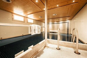 Ein Wellnessbereich mit Holzbalkendecke, Whirlpool und gefliestem Boden.