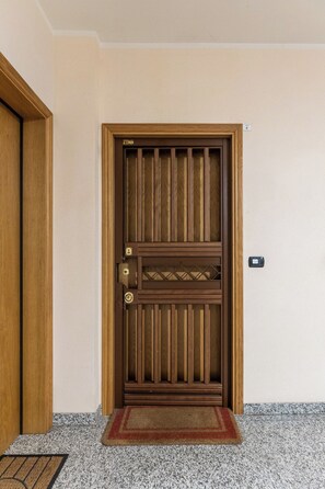 Eine Holztür mit vertikaler Paneelausstattung, eine Fußmatte und ein an der Wand befestigtes Gegensprechanlage.