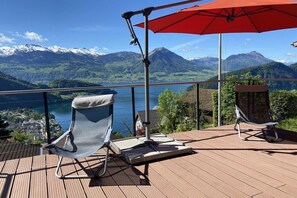 A deck with two chairs and a red umbrella, overlooking a lake and mountains. - Holiday home in Vitznau with swimming pool (Vitznau)