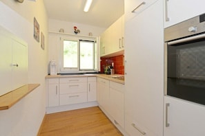 A compact kitchen with white cabinets, a built-in oven, and a window with a view of greenery outside. - Holiday home in Vitznau with swimming pool (Vitznau)