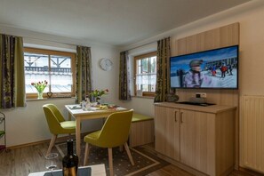 Ein Zimmer mit Esstisch, zwei Stühlen, Fernseher und einem fensterbepflanzten Fenster.