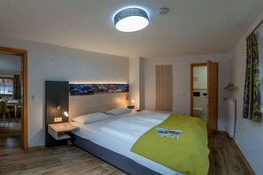 Ein modernes Schlafzimmer mit Bett, Nachttischen, einer Deckenleuchte und Blick ins Freie.