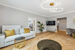 Moderni olohuone, jossa on sohva, televisio, huonekasvi ja kalanruotokuviollinen lattia.