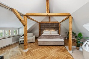A bedroom with a wooden ceiling structure, a bed, a sofa, a radiator, and a window. - Residence Hugo - Penthouse Apartment (Bad Schandau)