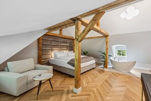 A bedroom with a bed, a sofa, a small table, a bathtub, and wooden beams. - Residence Hugo - Penthouse Apartment (Bad Schandau)