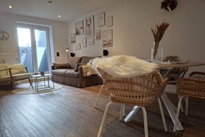 A modern living room with a sofa, chairs, a coffee table, and a dining table with a vase of dried plants. - Black-headed Seagull by DeJu Norderney (4**** DTV) (Norderney)