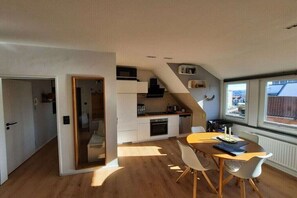 A compact kitchen with modern appliances, a dining area with a table and chairs, and a view through a window. - Möwennest by DeJu Norderney (3*** DTV) (Norderney)