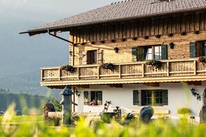 Eine traditionelle Holzhütte mit Balkon, Steinfundament und Blick auf die umliegende Landschaft.