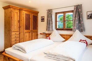 Ein Schlafzimmer mit zwei Betten, einem Holzschrank, einem Fenster mit Vorhängen und Blick ins Grüne.