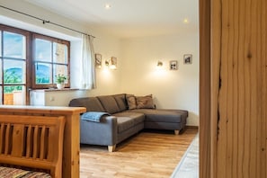Ein gemütliches Wohnzimmer mit einer Holzbank, einem grauen Sofa und einem Fenster mit Blick auf Grünflächen.