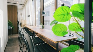 Un intérieur moderne avec une table en bois, des chaises noires, une plante en pot et de grandes fenêtres.