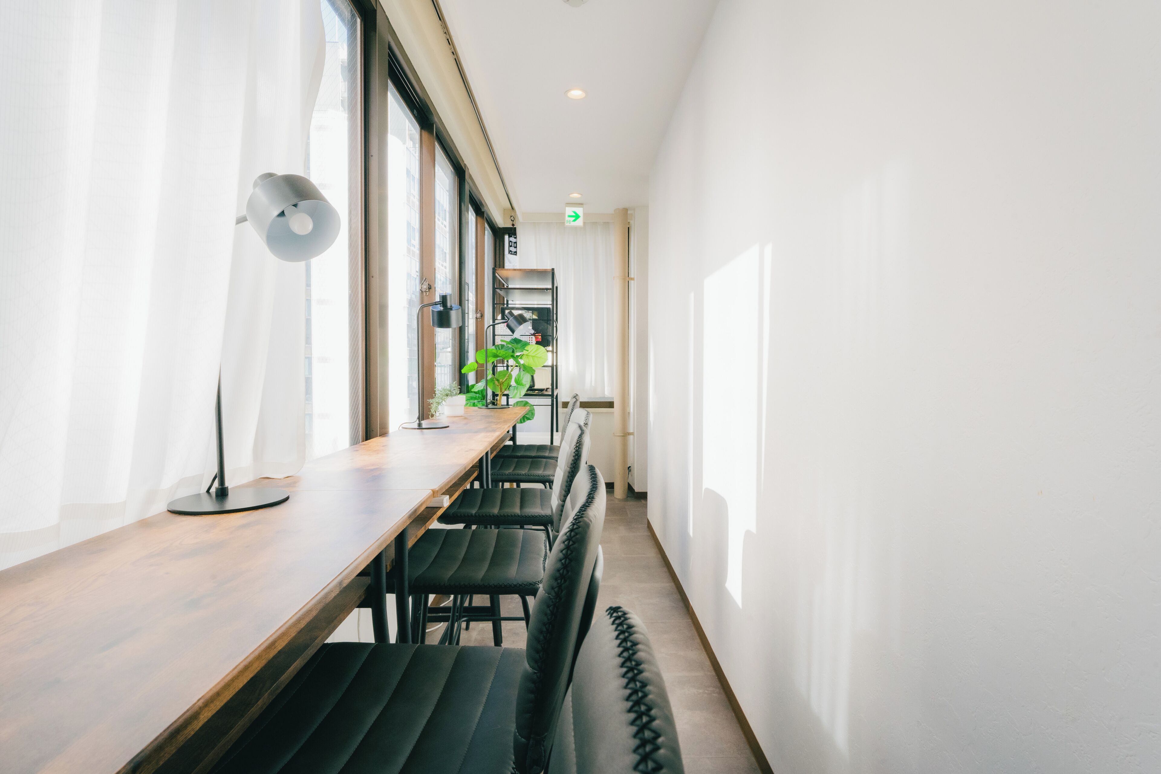 A corridor with a long wooden table, black cushioned seating, and a potted plant.