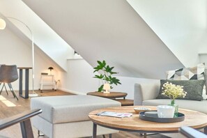 Ein modernes Schlafzimmer im Loft-Stil mit schrägen Wänden, einem runden Holztisch, einer Couch, einem kleinen Beistelltisch und einem Blumentopf.