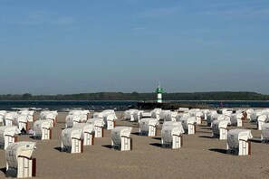 Ein Strand mit Reihen weißer Strandhütten, ein Leuchtturm im Hintergrund und ein klarer Himmel.