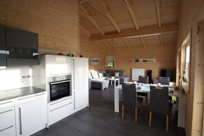 A modern kitchen with white cabinets and a built-in oven, a dining area with a table and chairs, and a living space with a sofa and a television. - Holiday home in Rieden with swimming pool (Rieden)