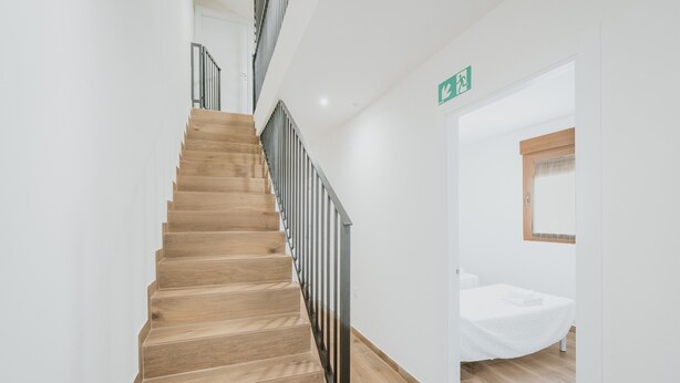 Een houten trap met een metalen leuning die leidt naar een kamer met een bed en een raam.