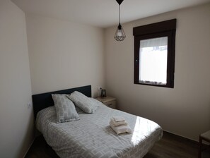 A bedroom with a bed, pillows, a bedside table, a lamp, and a window.
