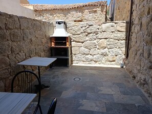 A stone-walled outdoor area with a built-in wood-fired oven, a table, and a chair.