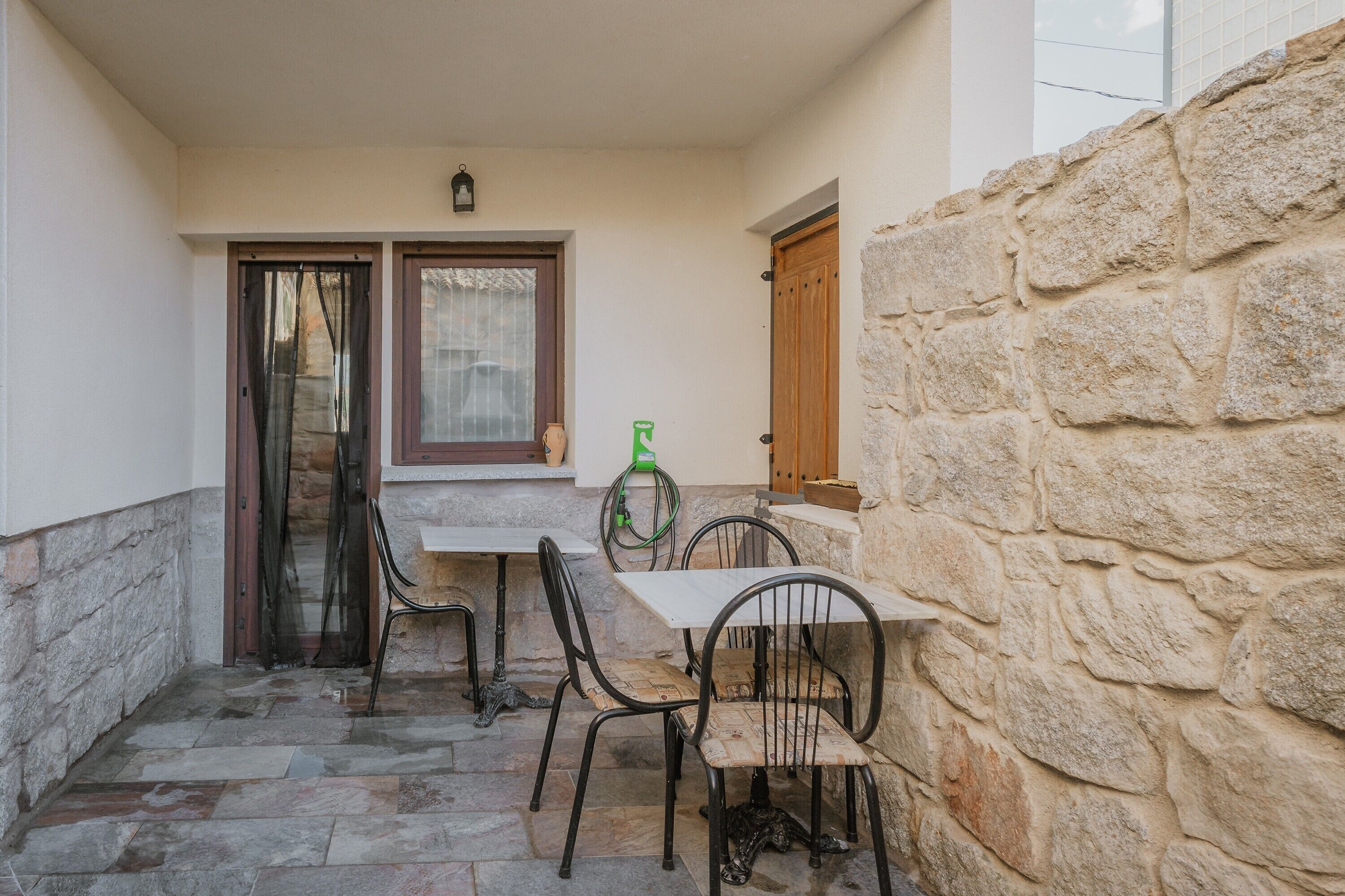 A stone-walled patio with a table and chairs, a door, and a window with curtains.