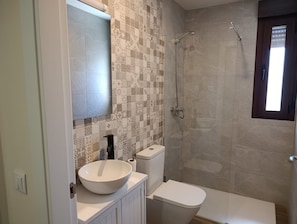A bathroom with a patterned tile wall, a white sink, a toilet, and a shower with a window.
