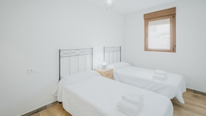 Een slaapkamer met twee bedden, een nachtkastje met een lamp, een raam en een hanglamp.