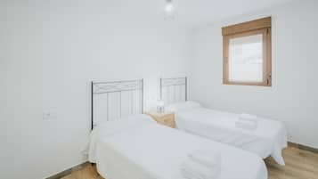 Et soveværelse med to senge, et natbord med lampe, et vindue og en pendel.